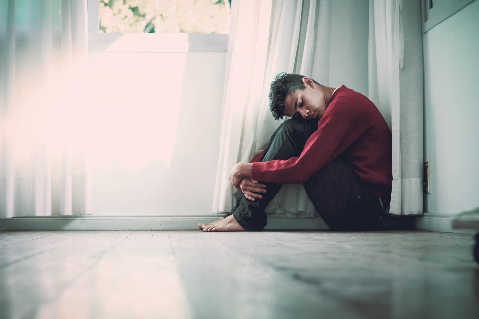 A man is sitting on the floor hugging his knee, likely experiencing anxiety. Dr. Aurelie Lucette, Miami therapist, explains how to manage panic attacks and how panic disorder can be treated with CBT.