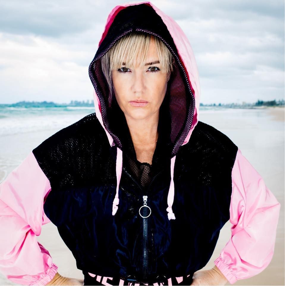 Woman wearing pink and black jacket, arms crossed, at beach.