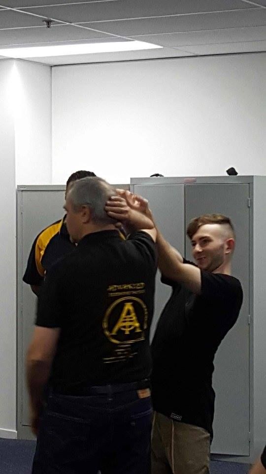 Man demonstrating a neck hold on another man indoors, possibly a self-defense lesson.