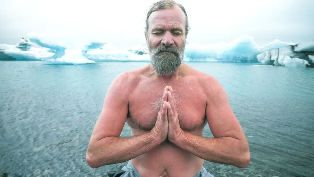 Man with beard meditates bare-chested by icy water, hands in prayer. Icebergs in the background.