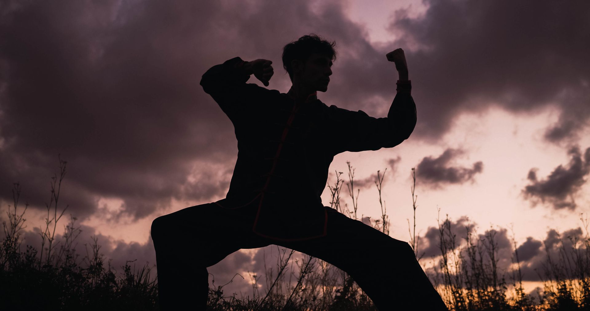 Silhouette of person in martial arts stance against a cloudy, colorful sunset.
