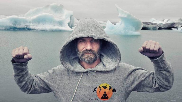 Man in gray hoodie raises fists, standing before iceberg-filled water.