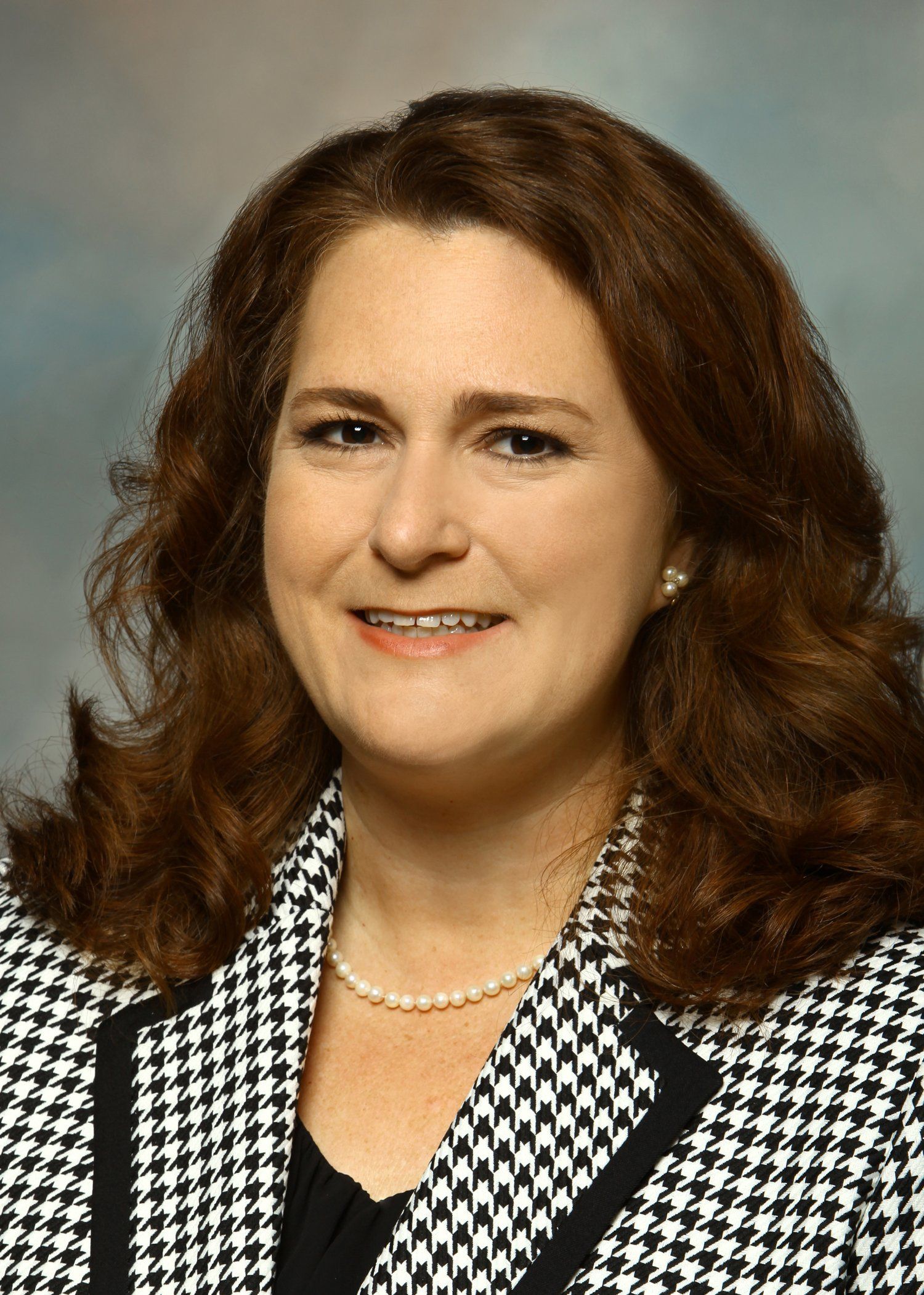 A woman is wearing a black and white jacket and a pearl necklace.