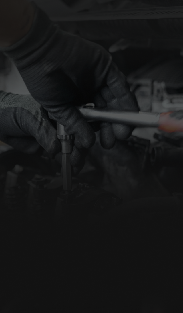 Hands in black gloves using a wrench on a car engine.