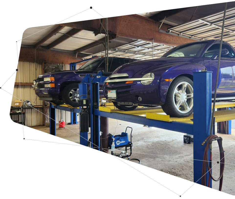 Two purple cars on a hydraulic lift inside an auto repair shop.