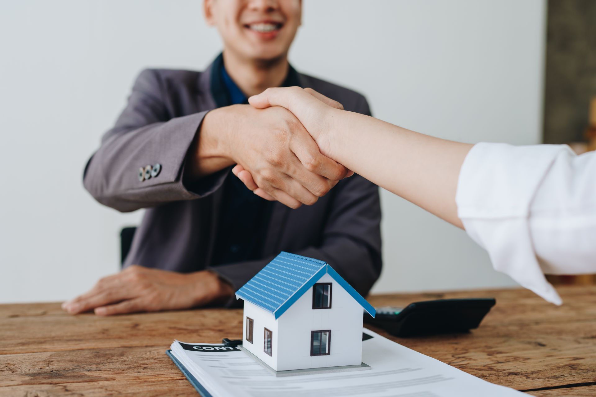 A cropped view of a lawyer shaking hands with a client over documents and a model home.