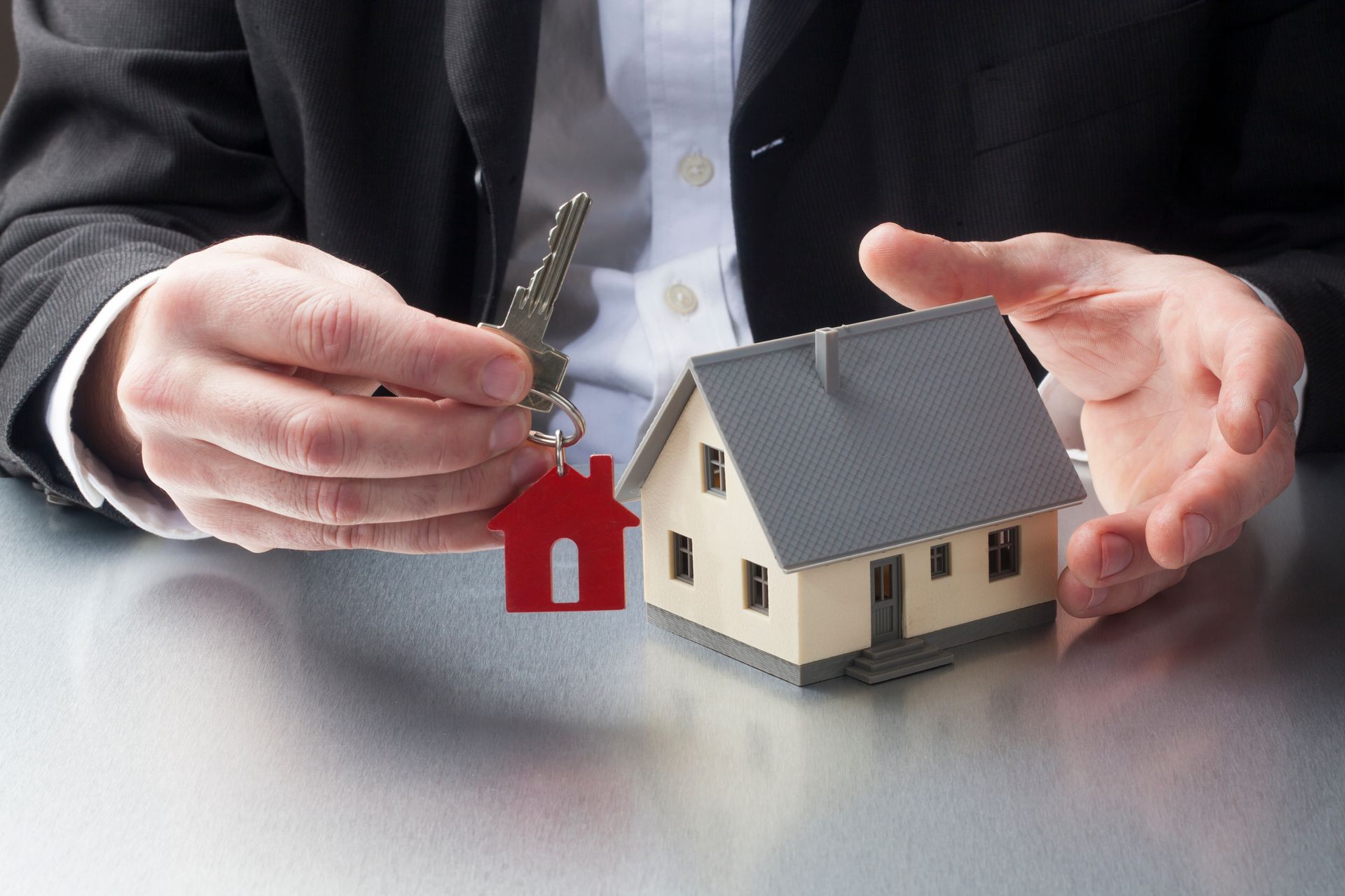 Image representation. A man in a suit with hands holding a house model and keys. Image representation. A man in a suit with hands holding a house model and keys.