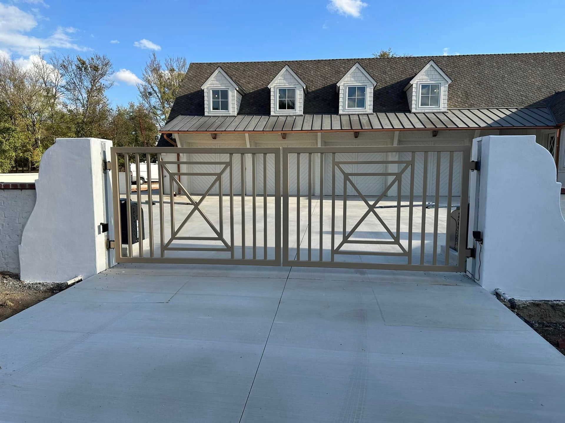 Gray metal gate in front of a building with white pillars and a concrete driveway.