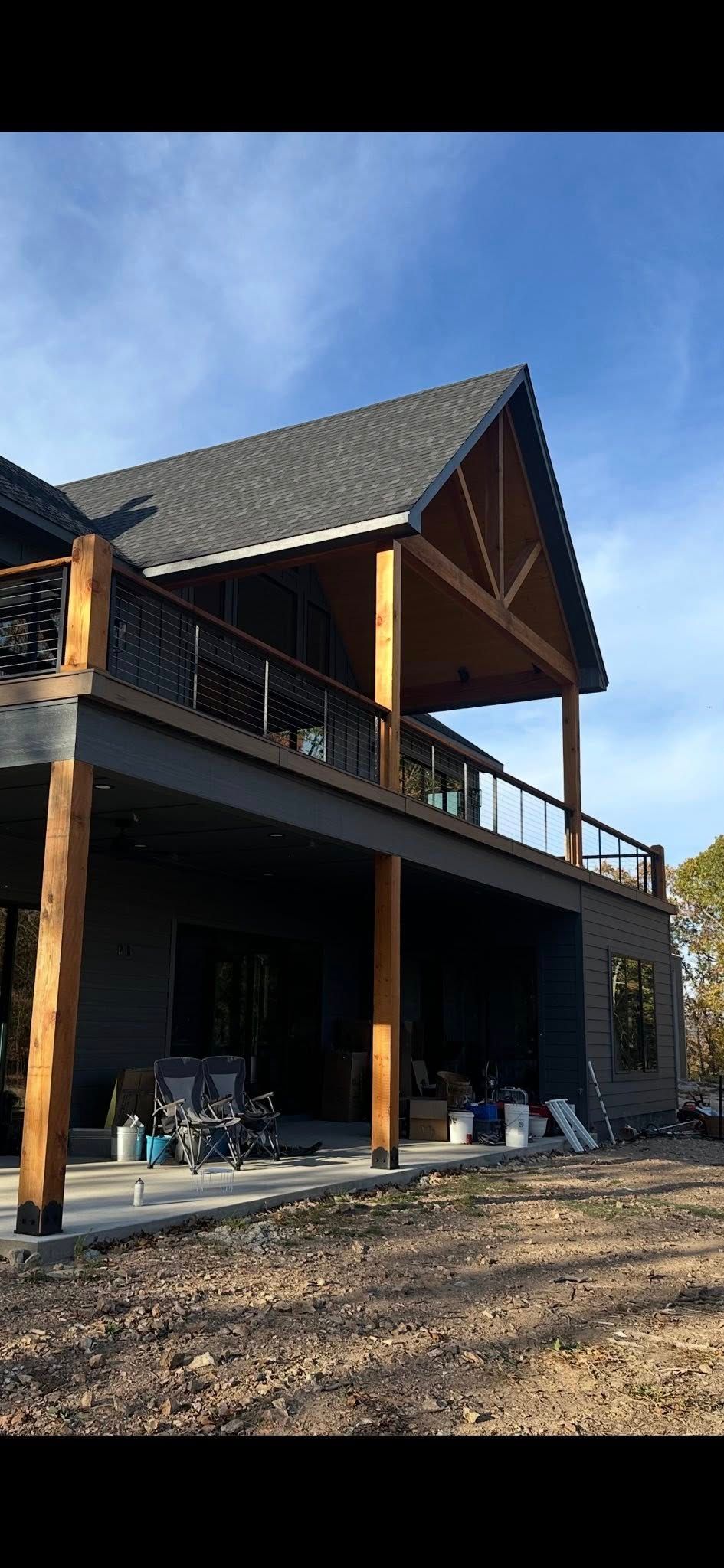 A two-story house with a wooden deck and supports, dark siding, and a gabled roof.