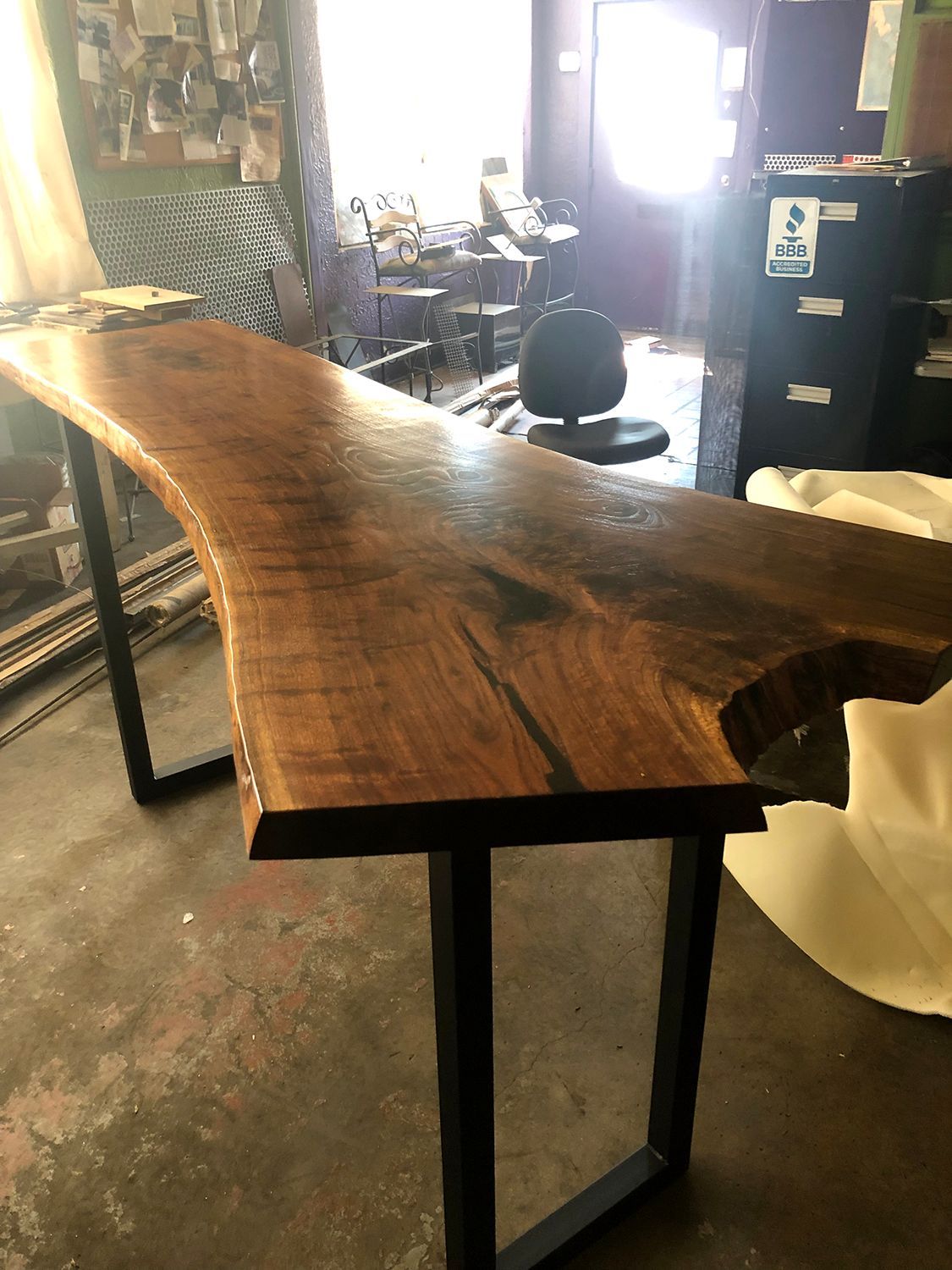 Live edge wood table with black metal legs in a workshop.