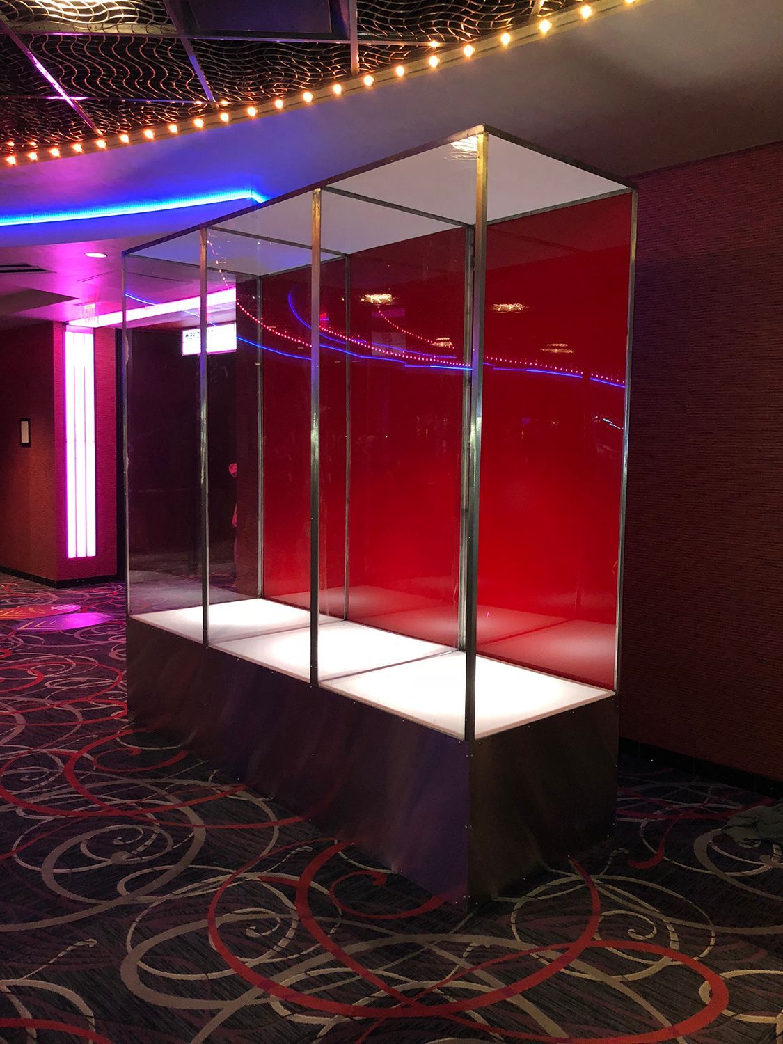 Empty display case in a corridor with red and white walls, chrome supports, and decorative carpeting.