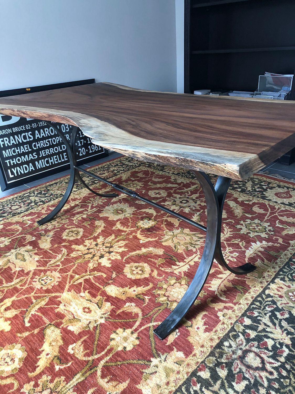 Wooden table with live edge and black metal legs on a red patterned rug.
