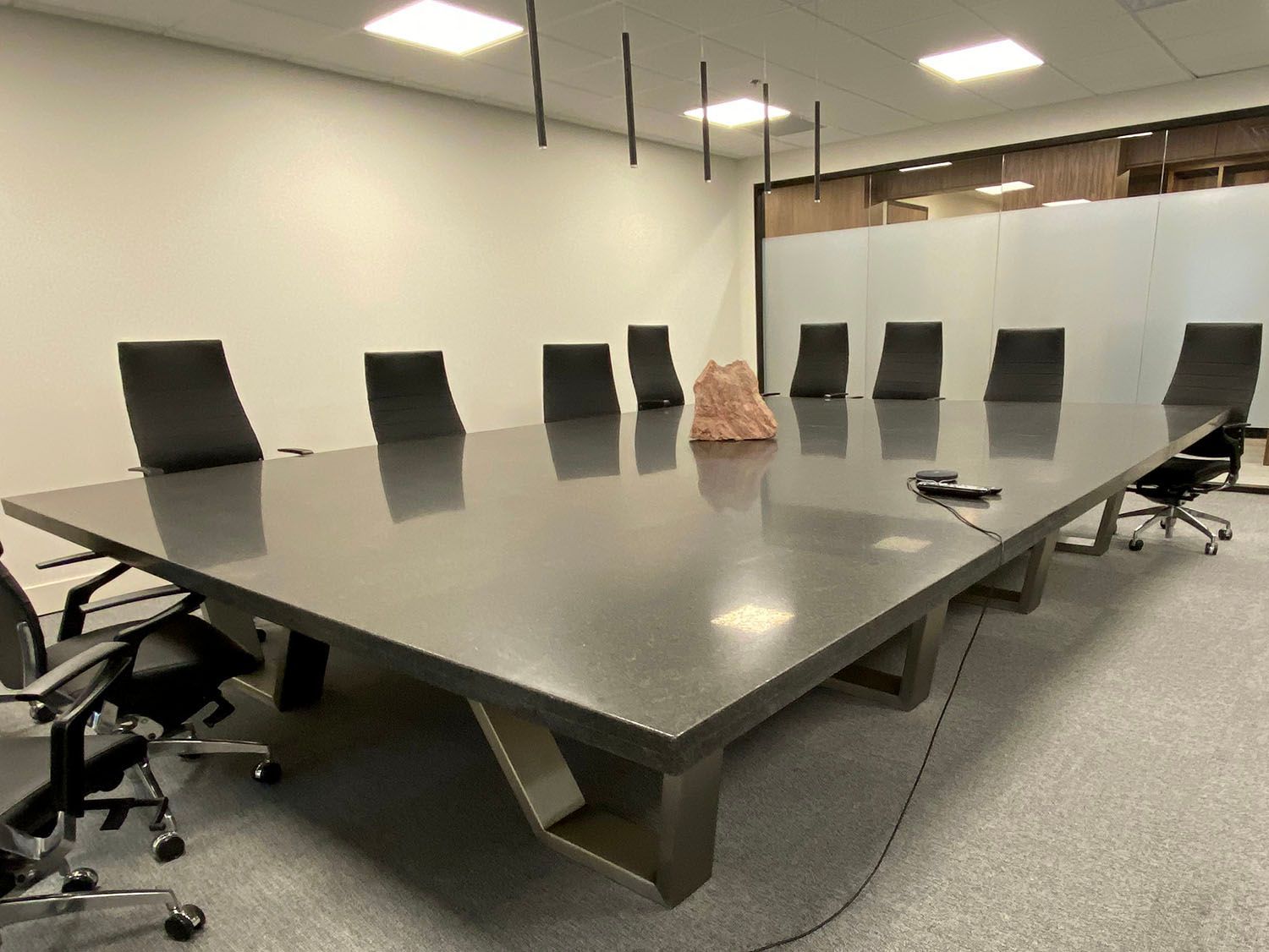 A large, grey rectangular conference table with black chairs in a modern office setting.