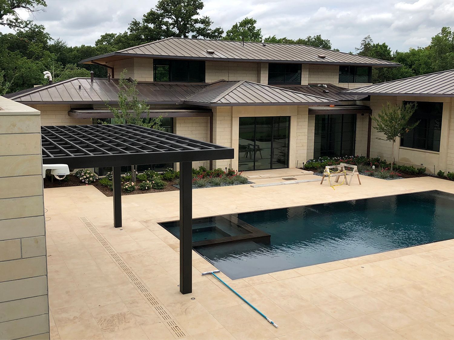 Luxury home with pool, patio, and pergola; brown metal roof; green trees in background.