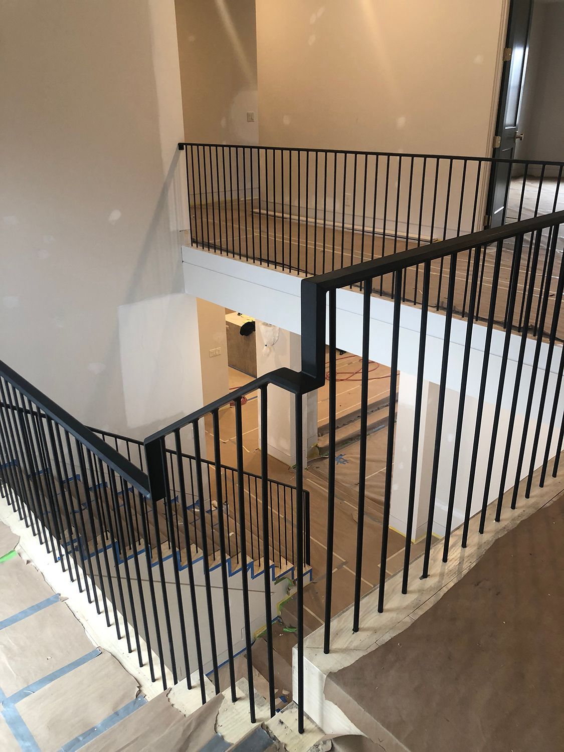 Black metal railing on a staircase with beige walls, viewed from above.