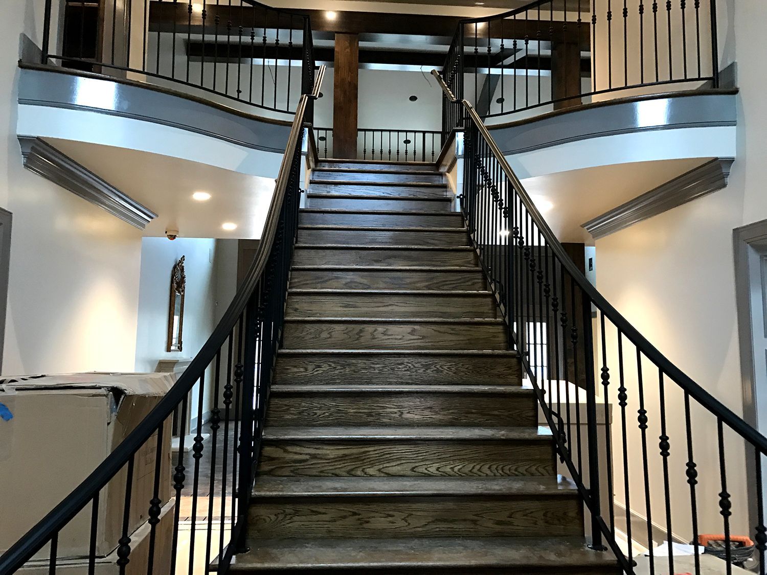 Wooden staircase with black railings, leading up to a second floor. Beige walls, recessed lighting, and a view of a landing.