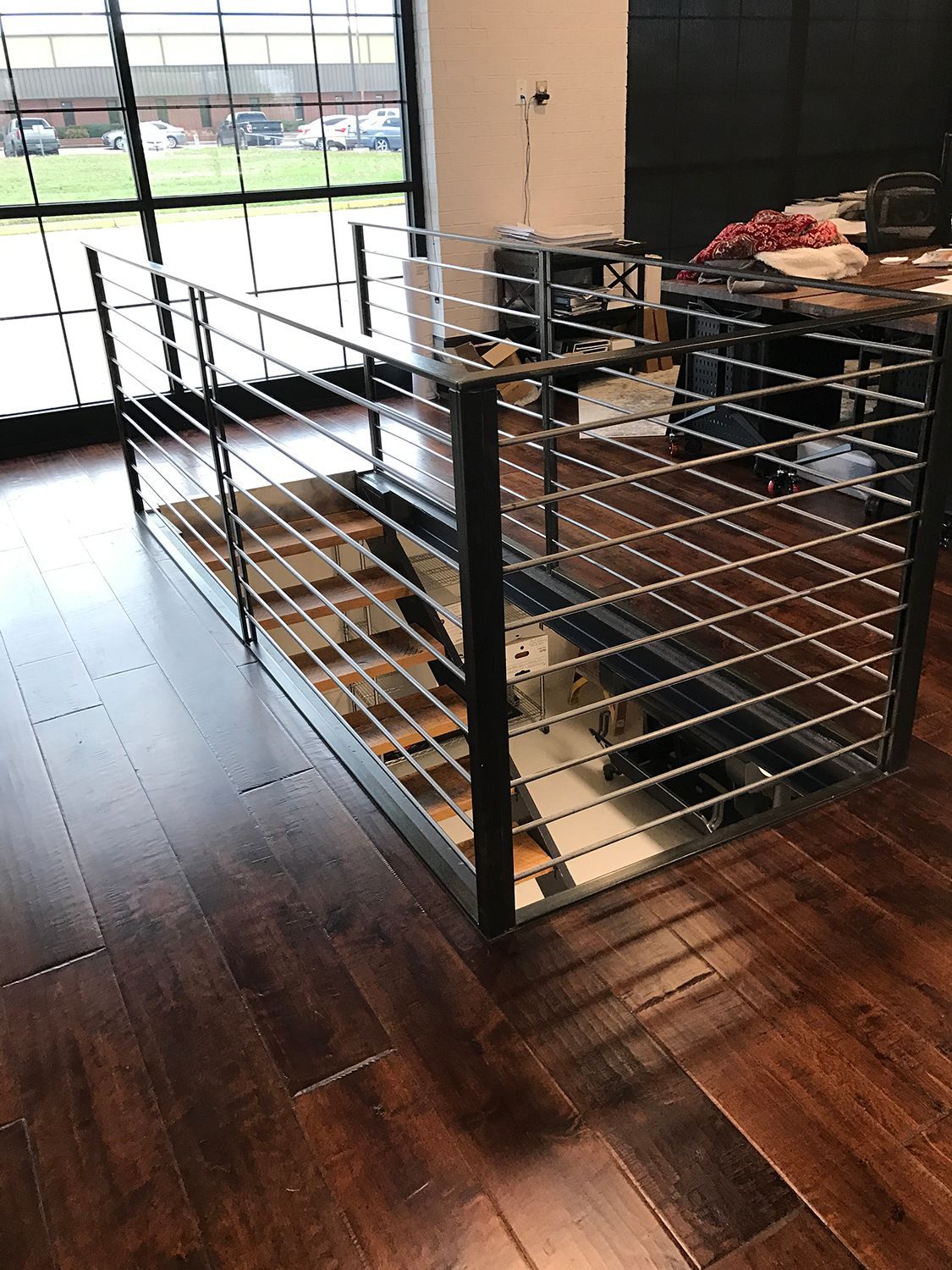 Modern metal railing surrounds a recessed floor area with wooden steps and a dark wooden floor.