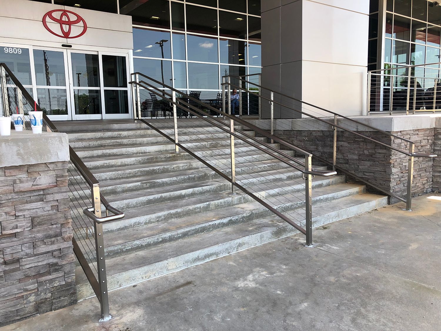 Exterior of a Toyota dealership with concrete steps and metal handrails leading to the entrance.