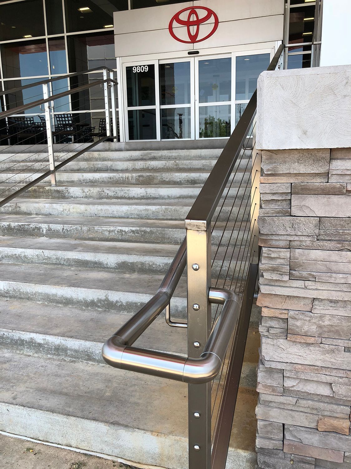 Entrance to a Toyota dealership with concrete steps and a stainless steel handrail.