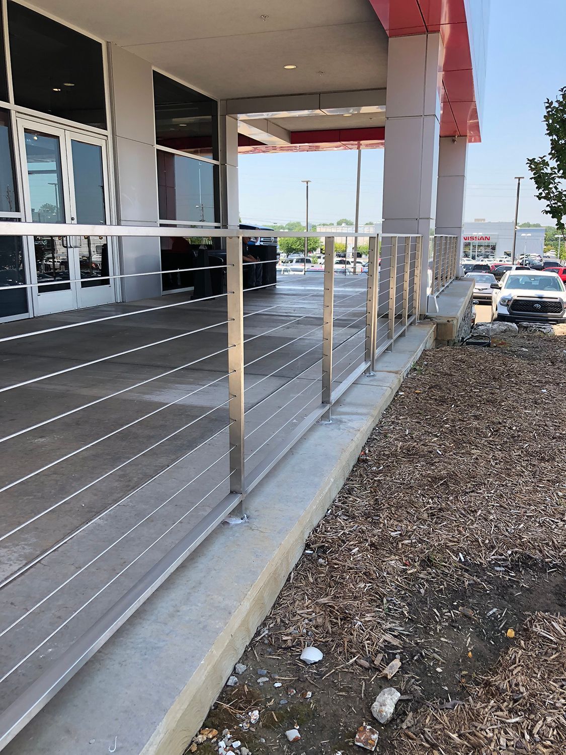 A low concrete wall and cable railing along a building entrance, leading to a parking area.
