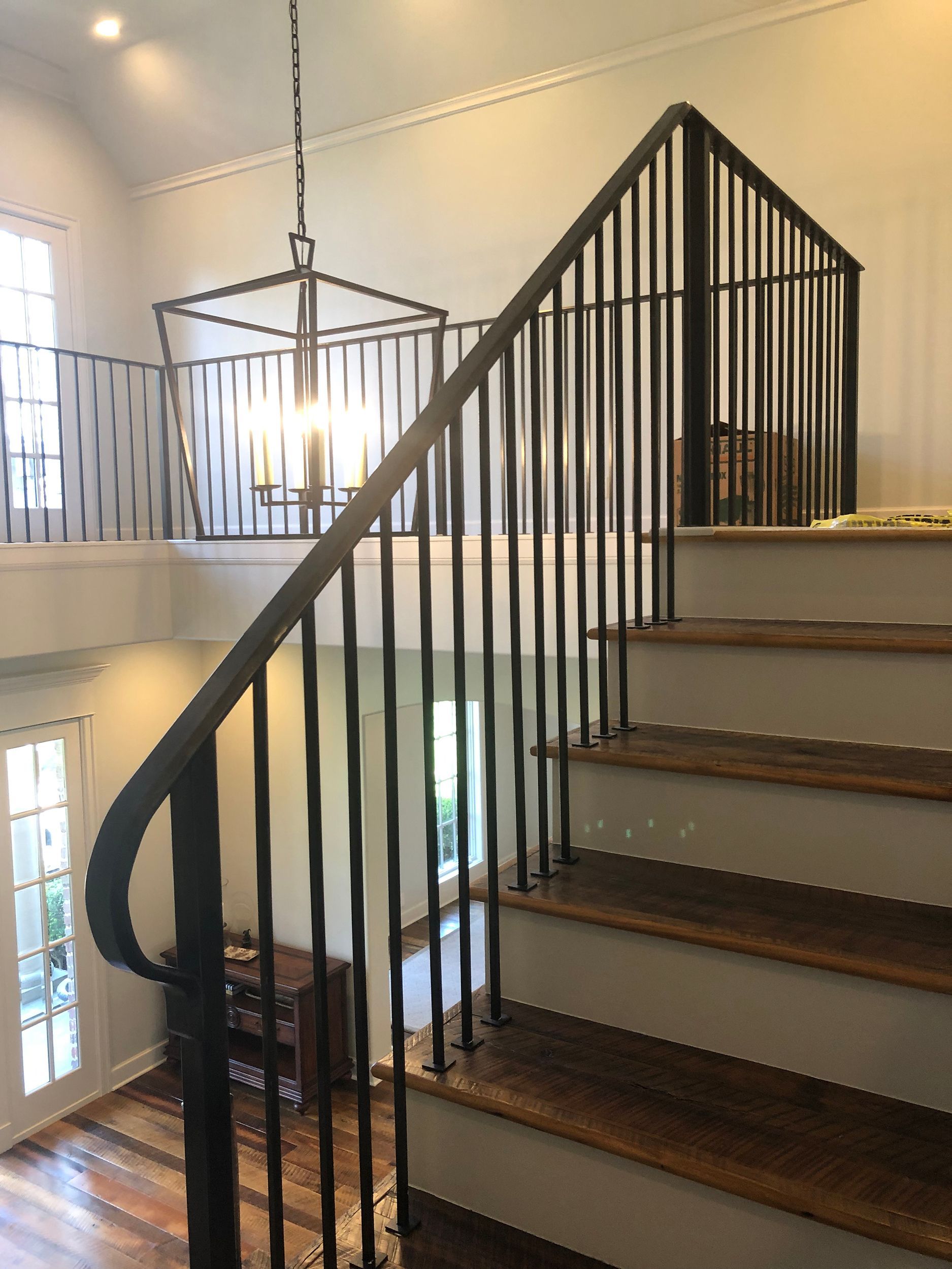 Staircase with dark metal railing, leading to a loft. A chandelier hangs above.