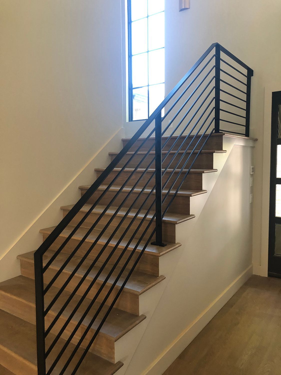 Staircase with wooden steps and black metal railings against a white wall.