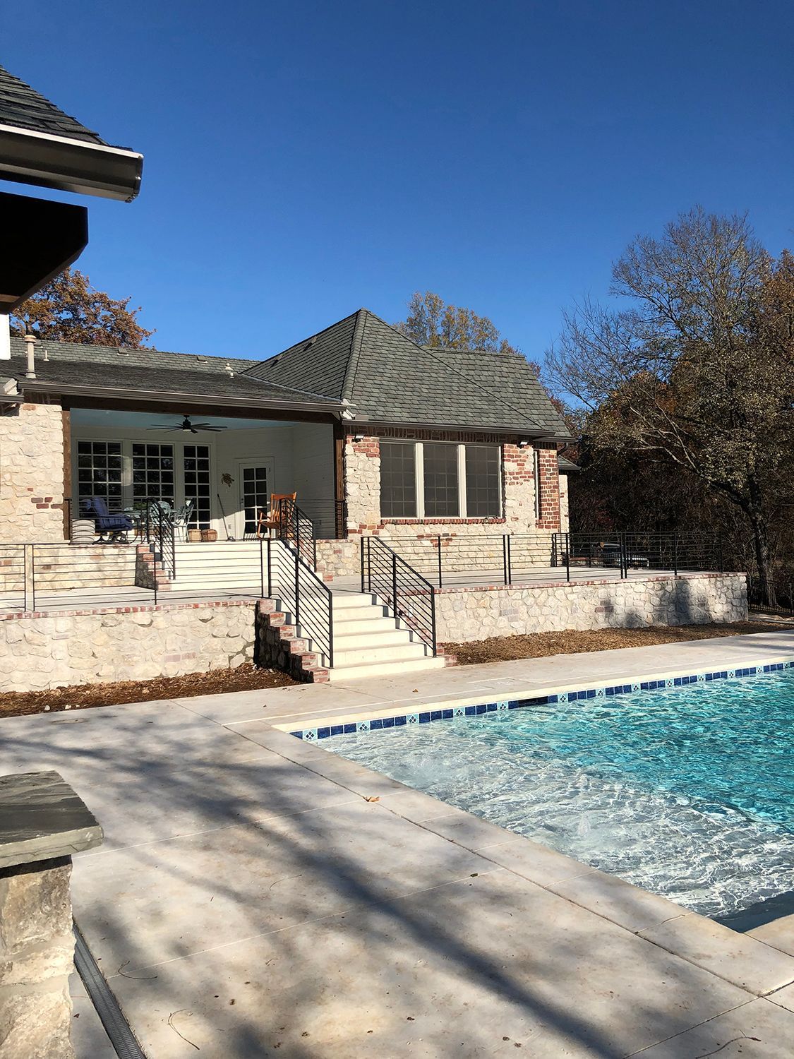 Poolside view of a brick house with stairs, a patio, and a pool. Bright blue sky.
