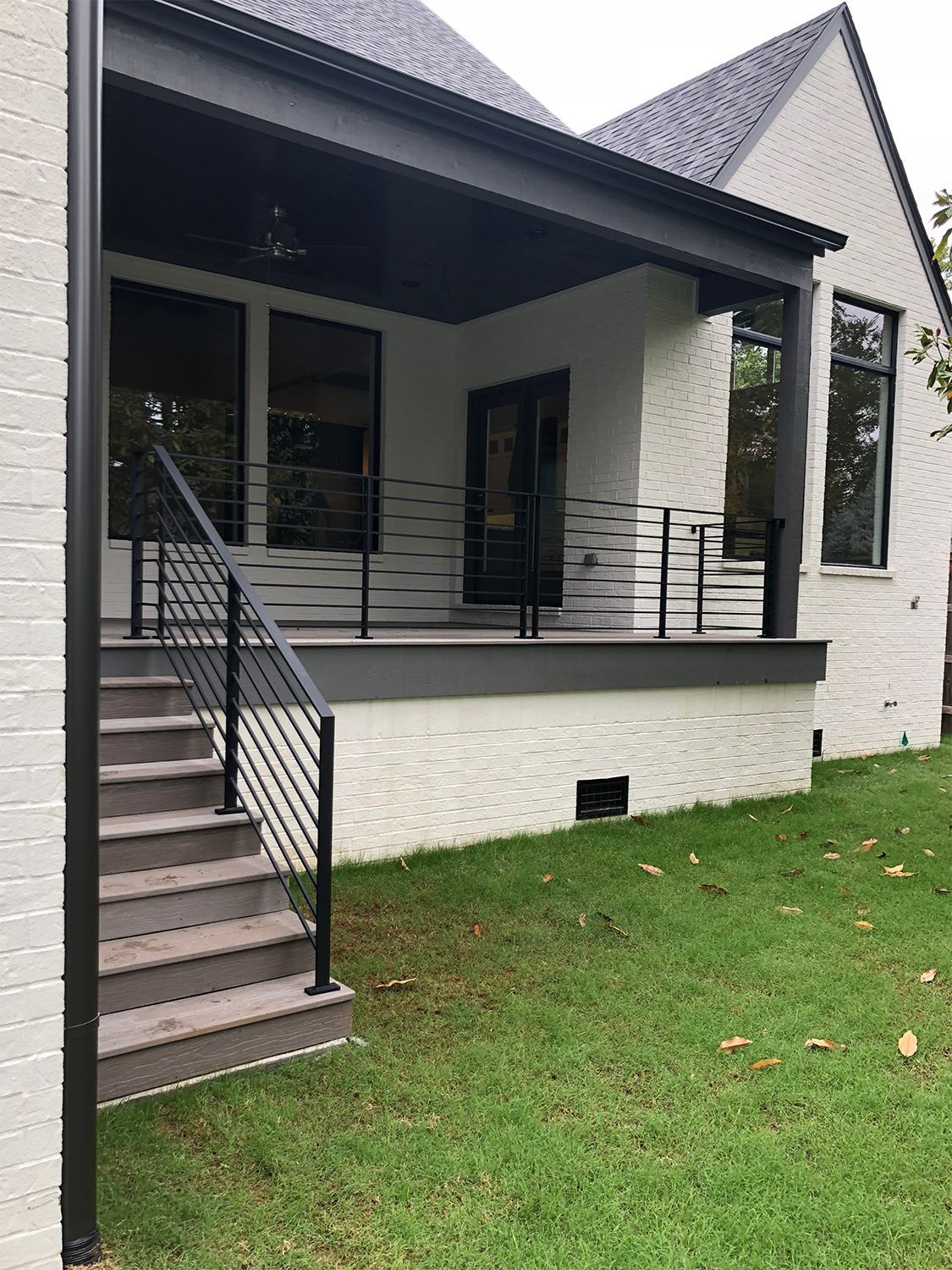 Exterior view of a white brick home with a covered porch and steps; black railing.