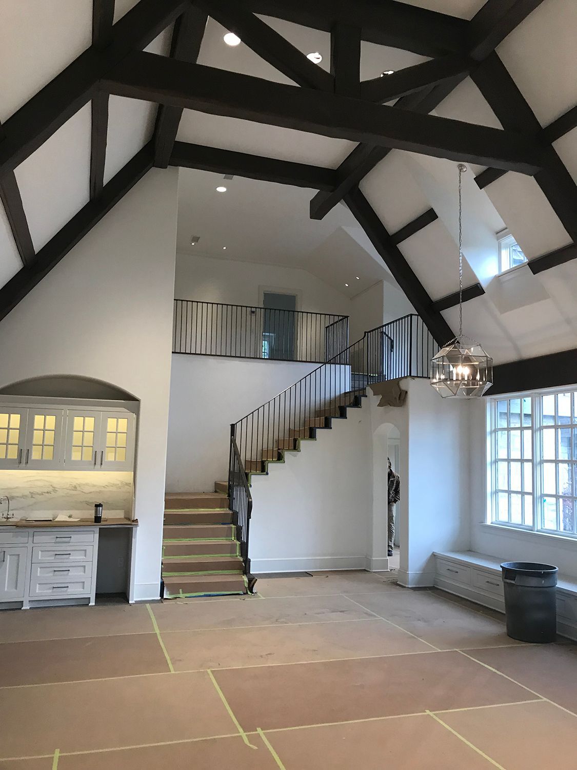 Interior view of a house with a staircase, loft, and exposed wooden beams.