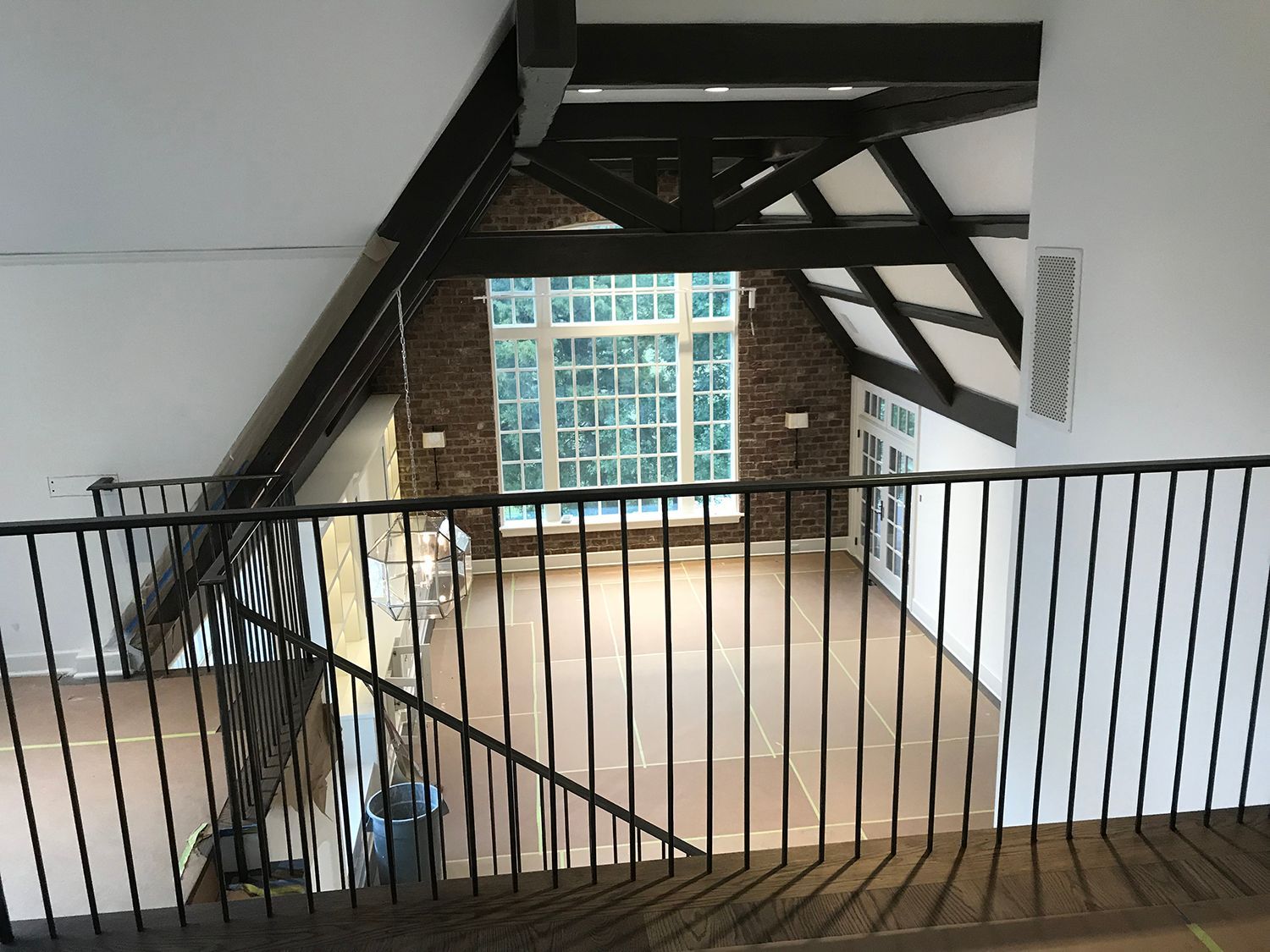 Interior view of a loft space with a large window, wooden beams, and a railing.