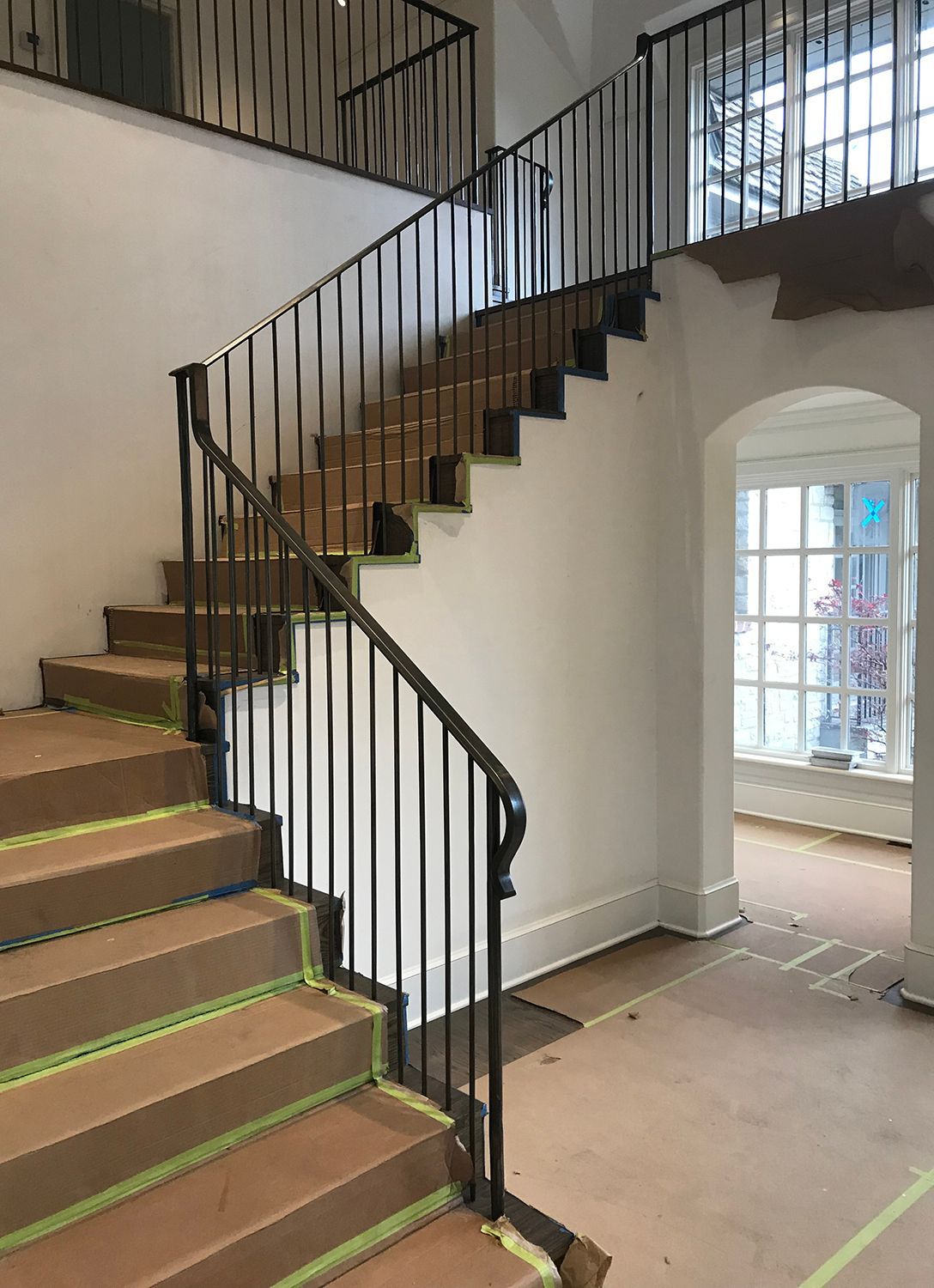 Staircase with brown cardboard on steps, black metal railing, and a window in a white-walled room.