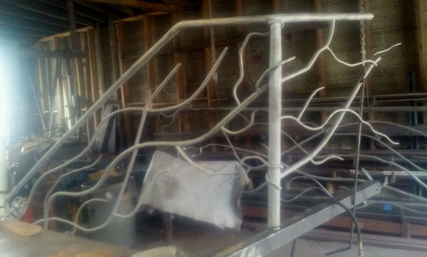 Metal staircase railing with an organic, branch-like design in a workshop.