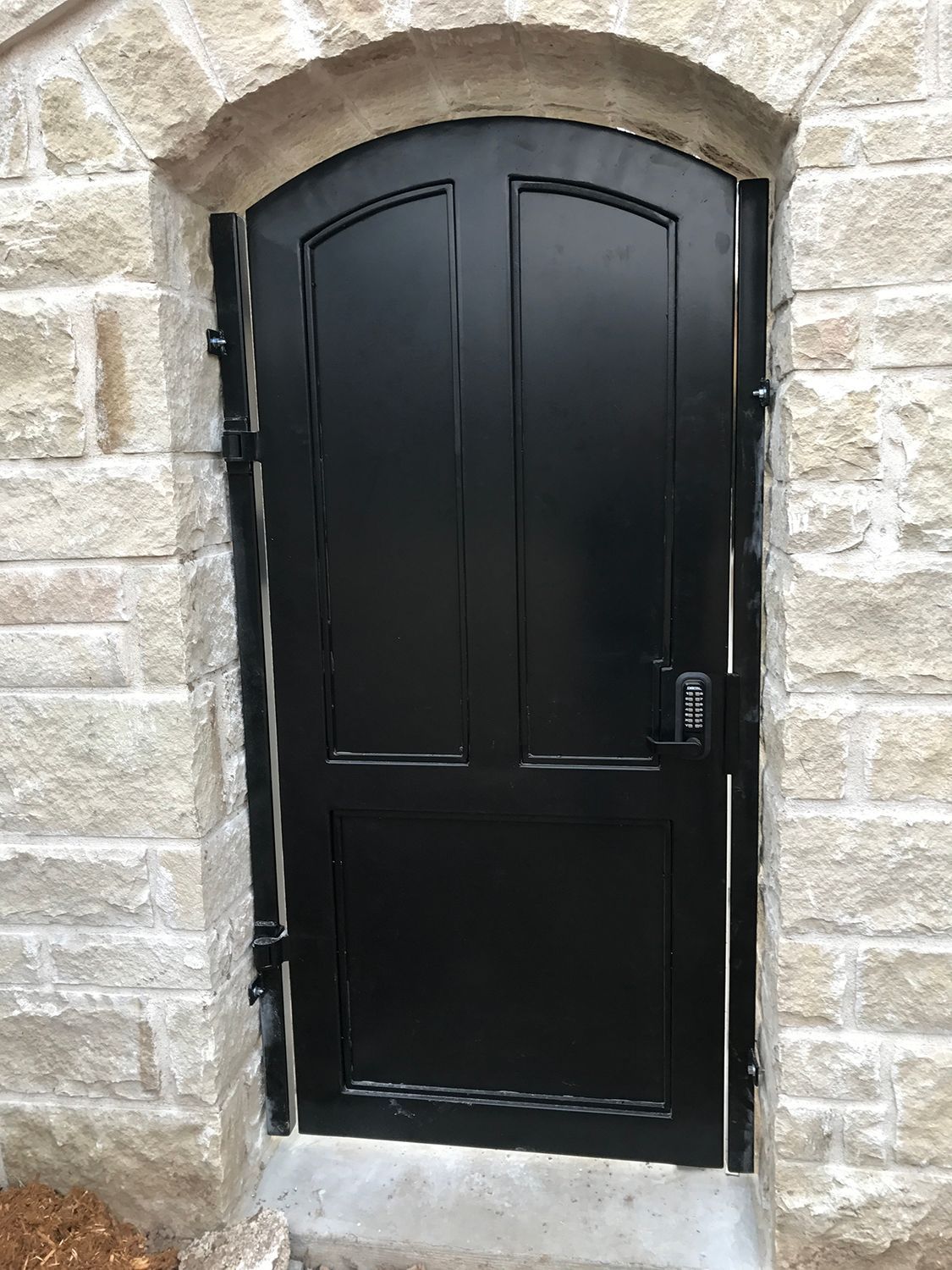 Black door with a keypad set in a stone archway.