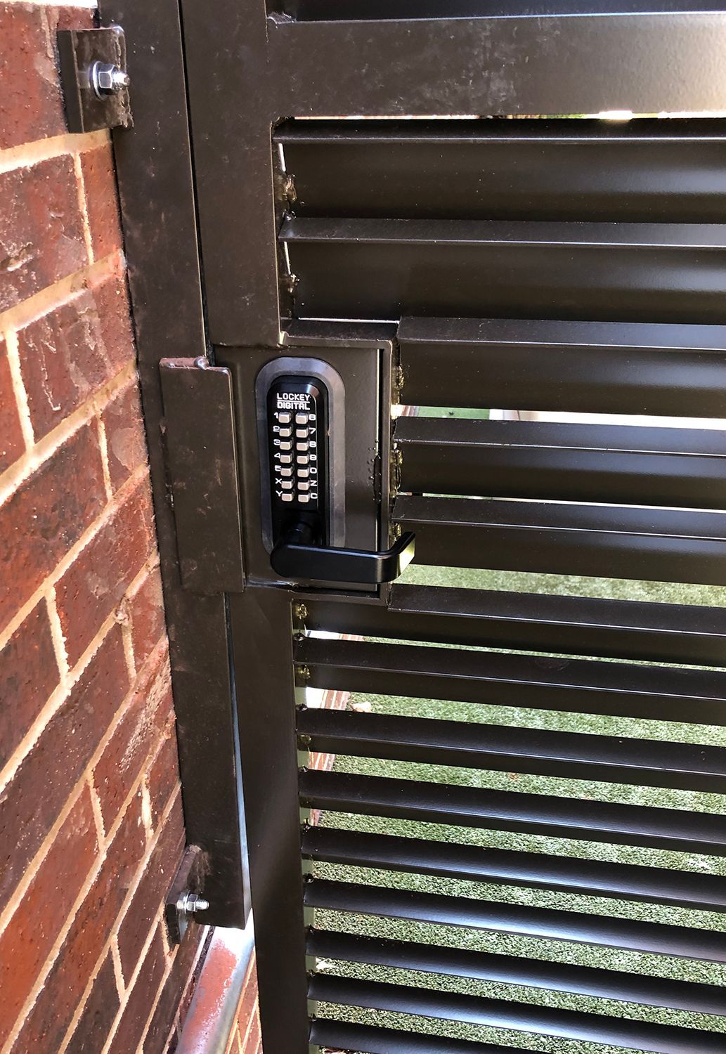 Black metal gate with a combination keypad lock attached to a brick wall.