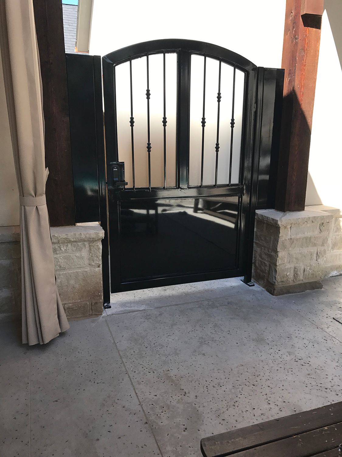 Black metal arched gate between two pillars on concrete surface.
