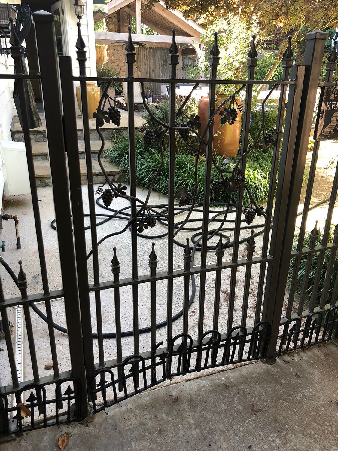 Black wrought iron gate partially open on a concrete surface, with a garden visible behind.