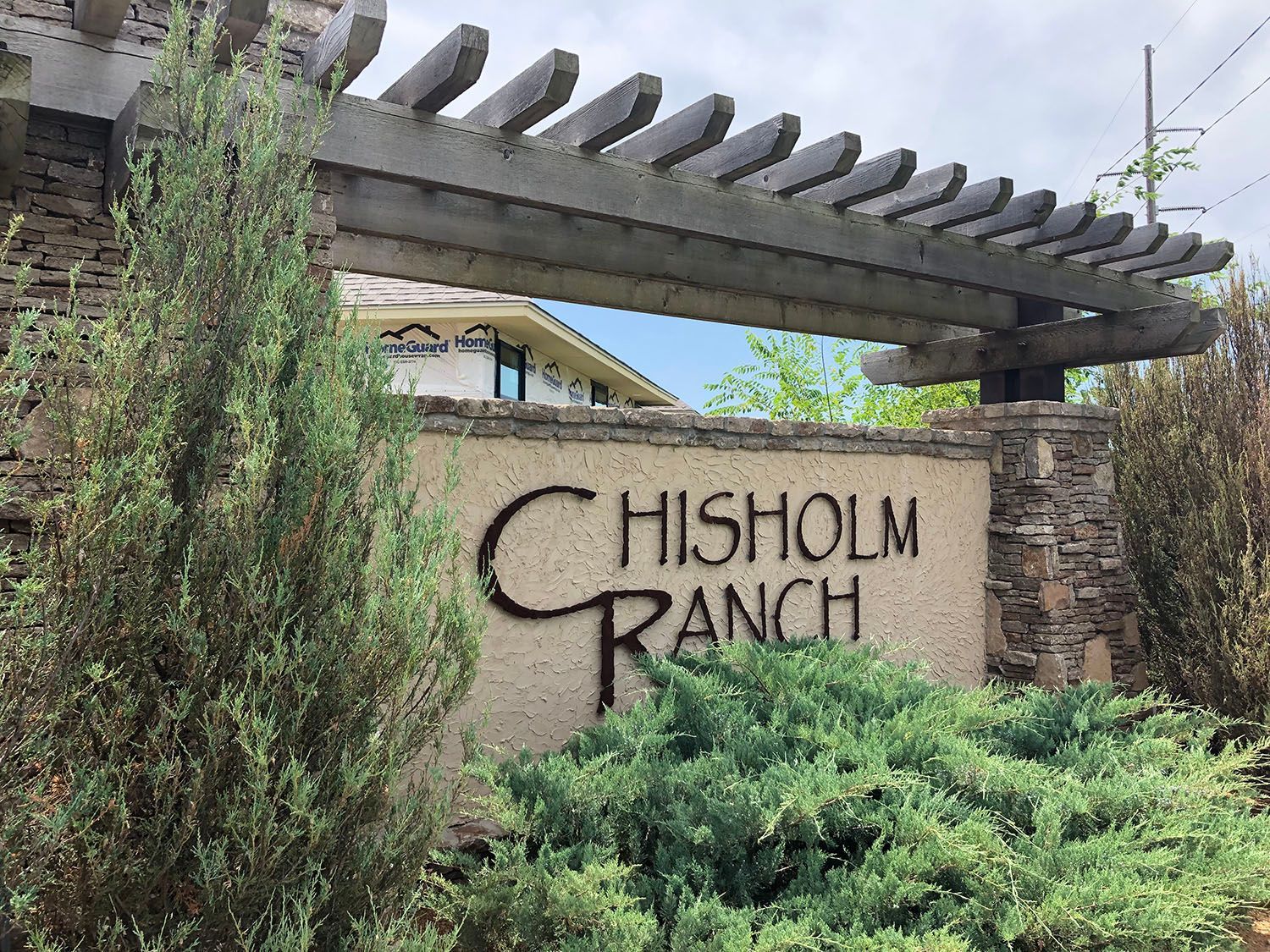 Chisholm Ranch entrance sign with stone pillars and wooden pergola, surrounded by greenery.