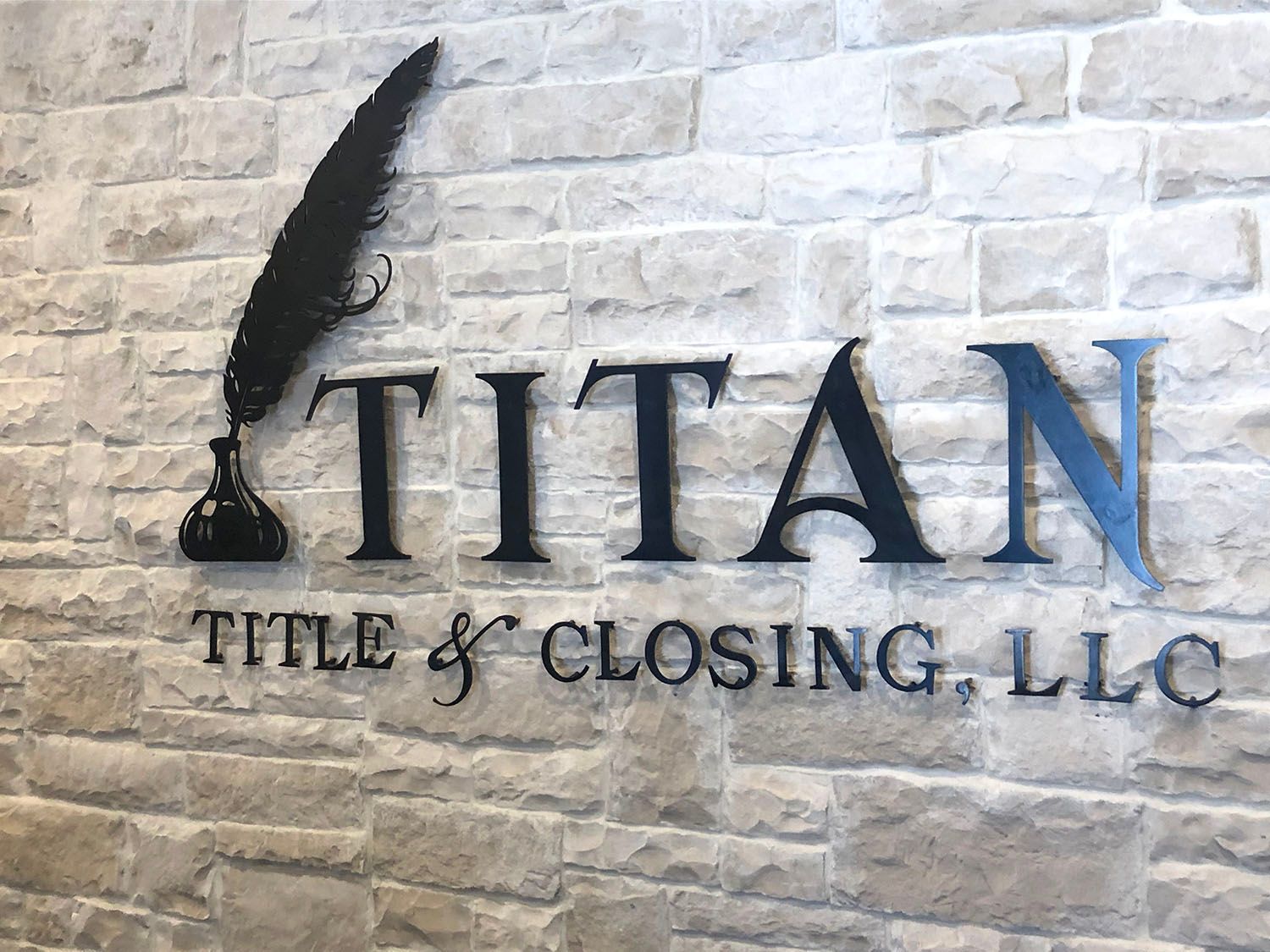 "Titan Title & Closing, LLC logo on a brick wall, featuring a quill and inkwell next to the company name."