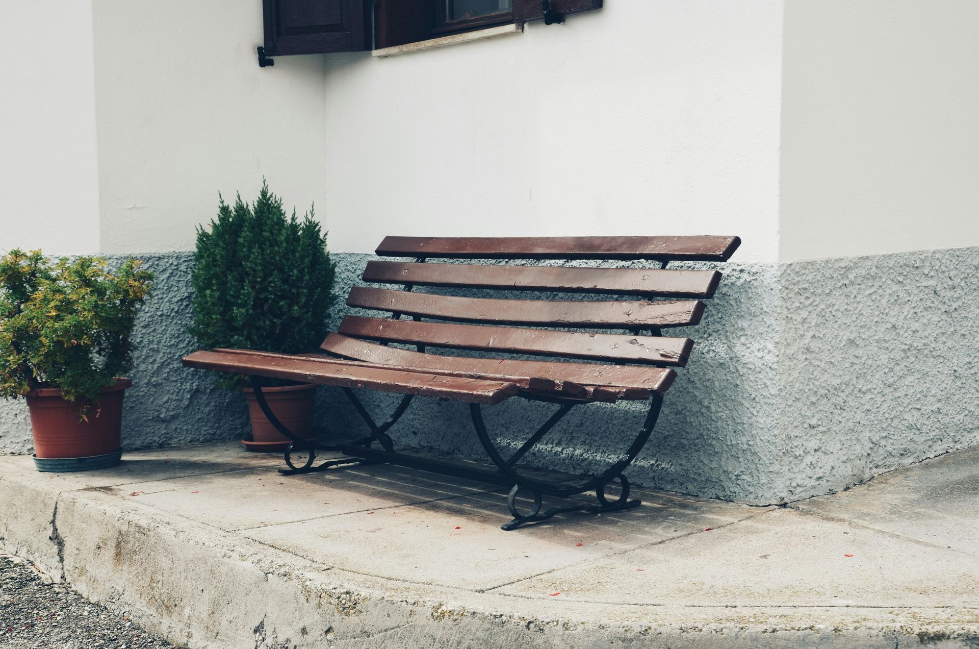Wooden bench beside a building with potted plants.