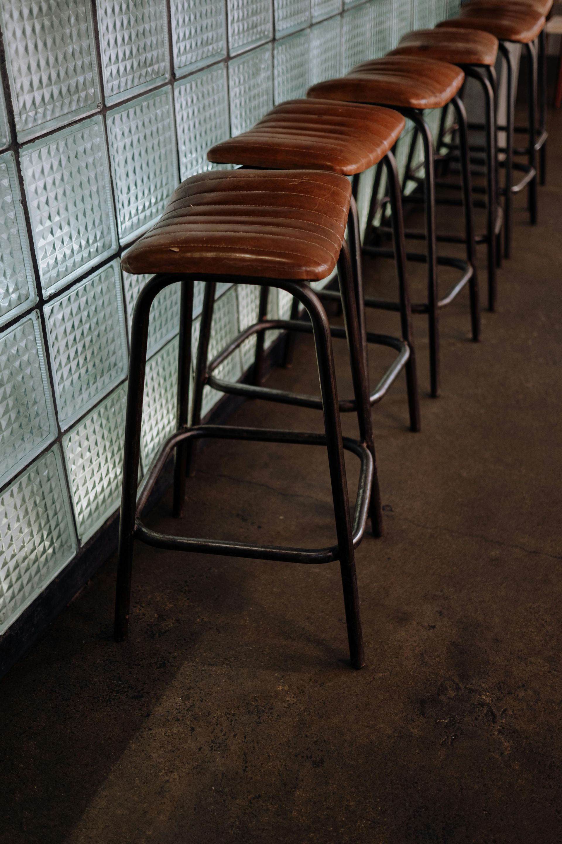 Row of brown leather bar stools against a textured glass wall.