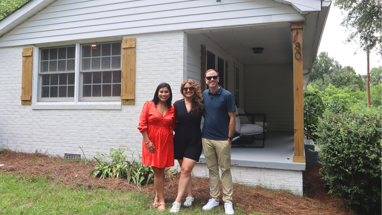 Three real estate investors smile in front of a newly renovated property