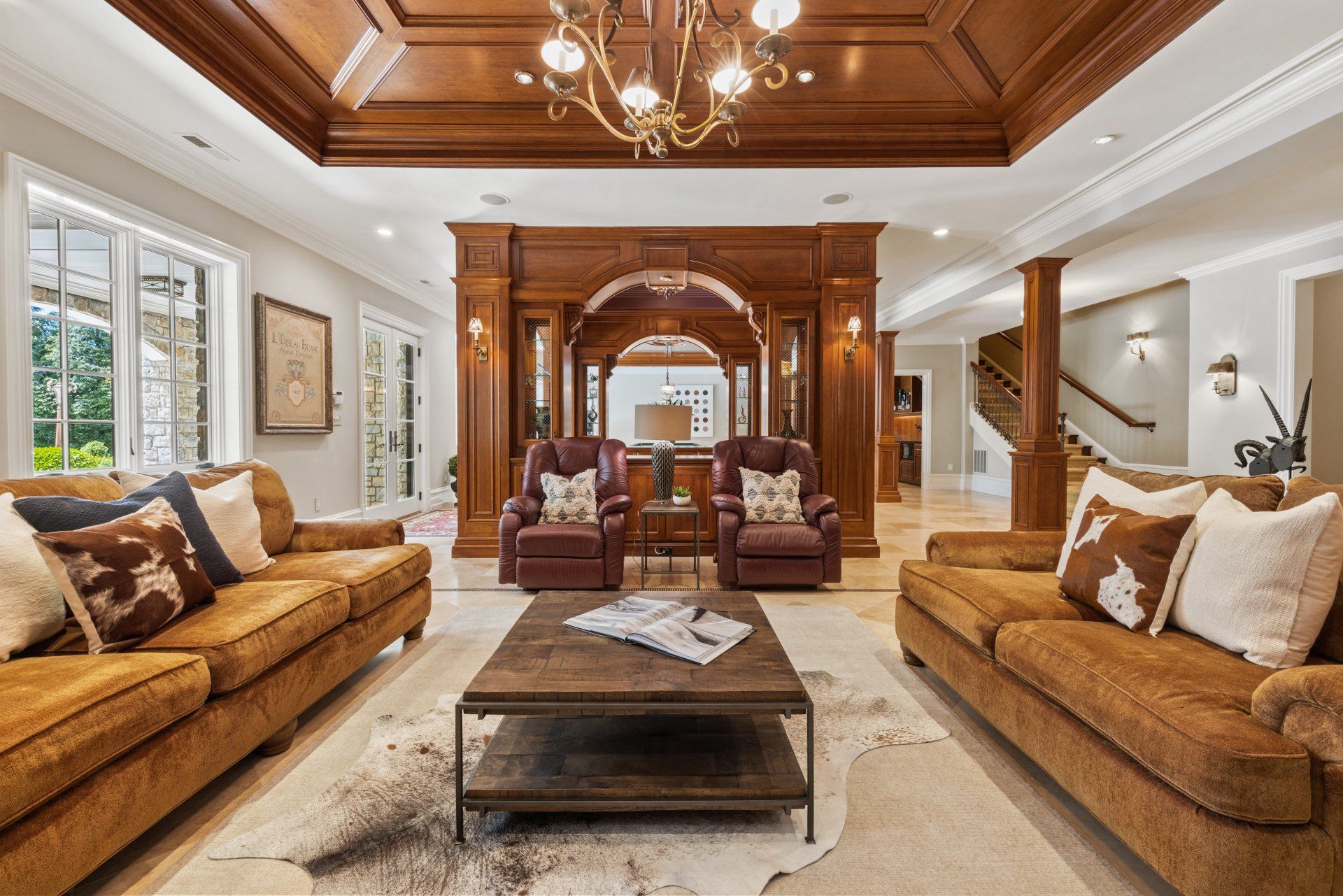 A luxurious living room with two couches , two chairs , a coffee table and a chandelier. Wood throughout including ceilings. Shoot by Craig Westerman. 