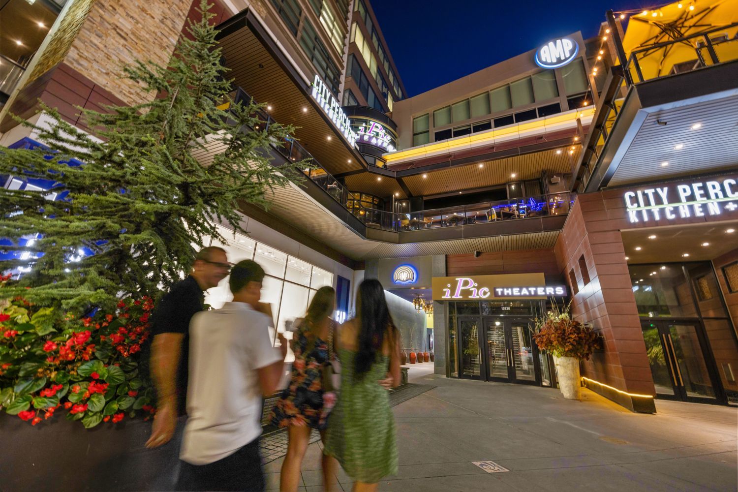 A group of people are walking down a sidewalk in front of a building in Downtown Bethesda in the evening. Shot by Craig Westerman