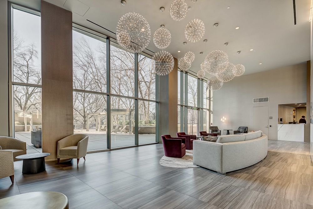 A large lobby with a couch , chairs , and a chandelier hanging from the ceiling. Photo shoot by Craig Westerman in Chevy Chase.
