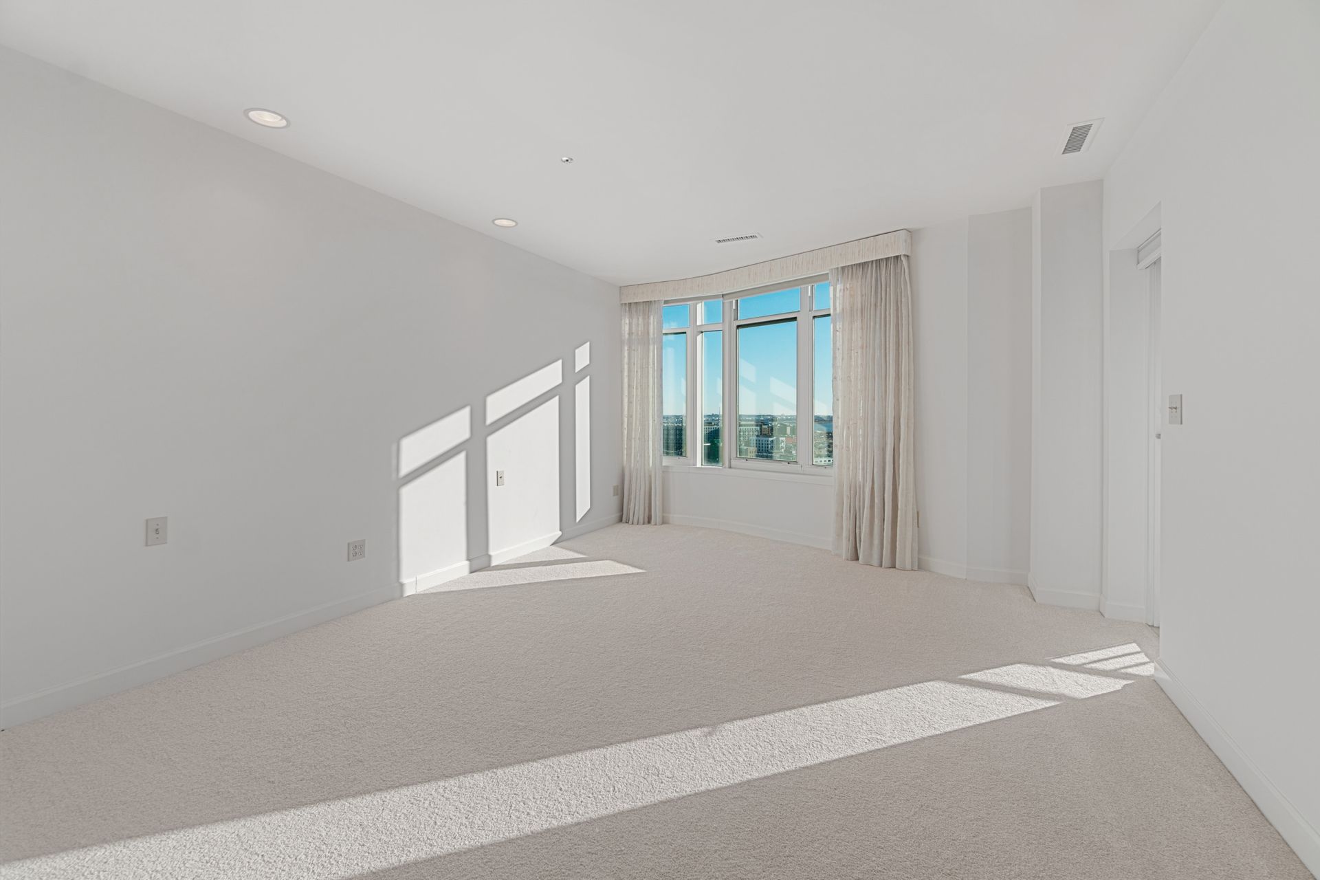 an empty room with a large window and a carpeted floor .
