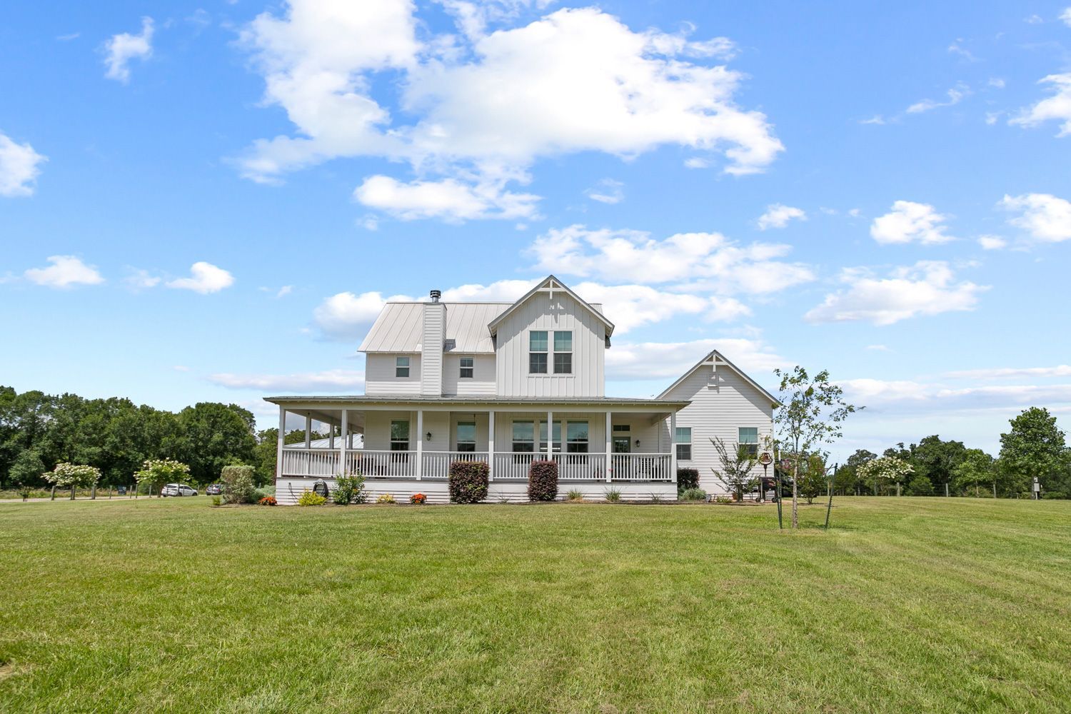 Long shot of large white house with a porch is sitting on top of a lush green field by craig westerman and team.