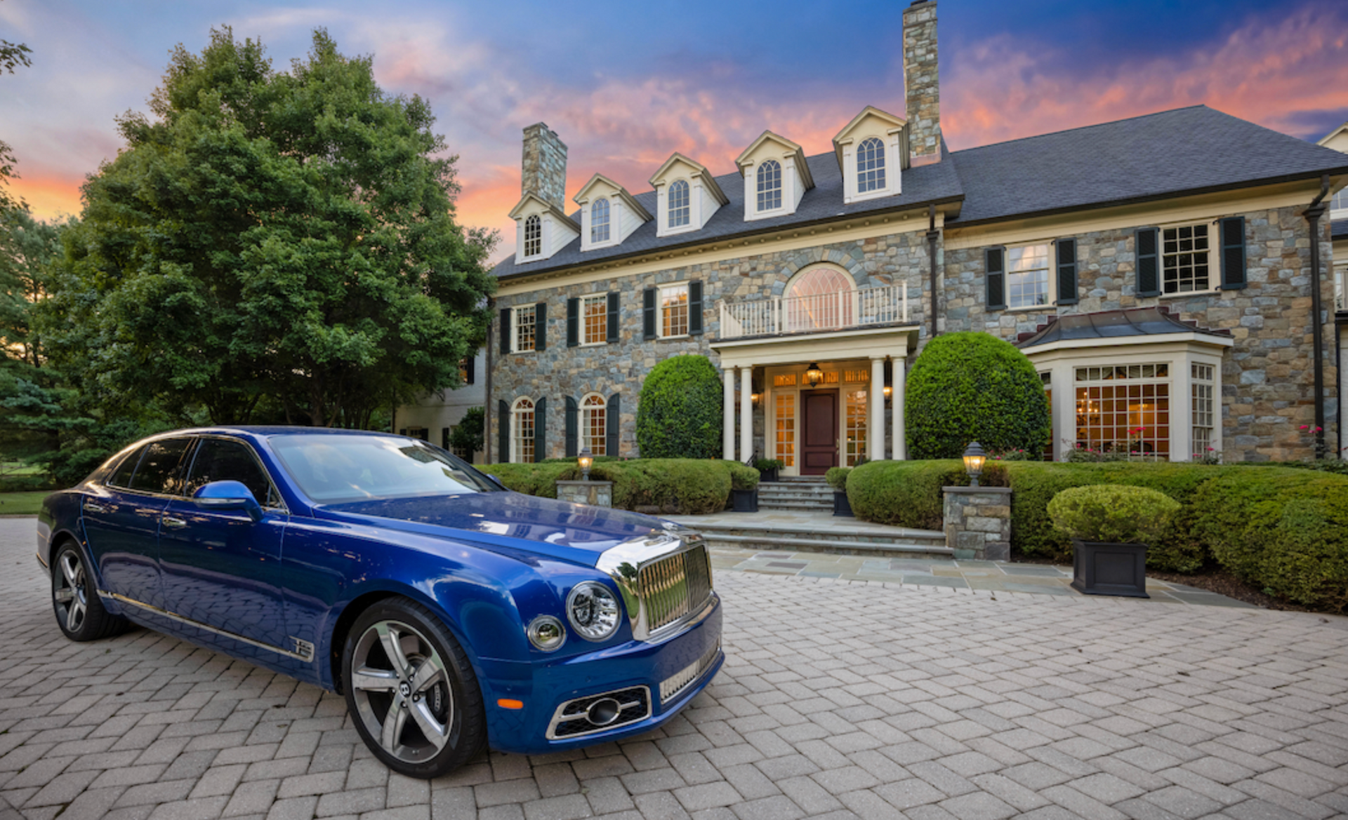 a blue luxury car is parked in front of a large stone house. photo by craig westerman