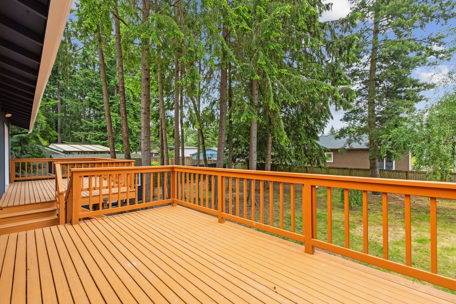 A beautiful large wooden deck with a wooden railing and trees in the background in Seattle, WA - shoot by Hometrack.