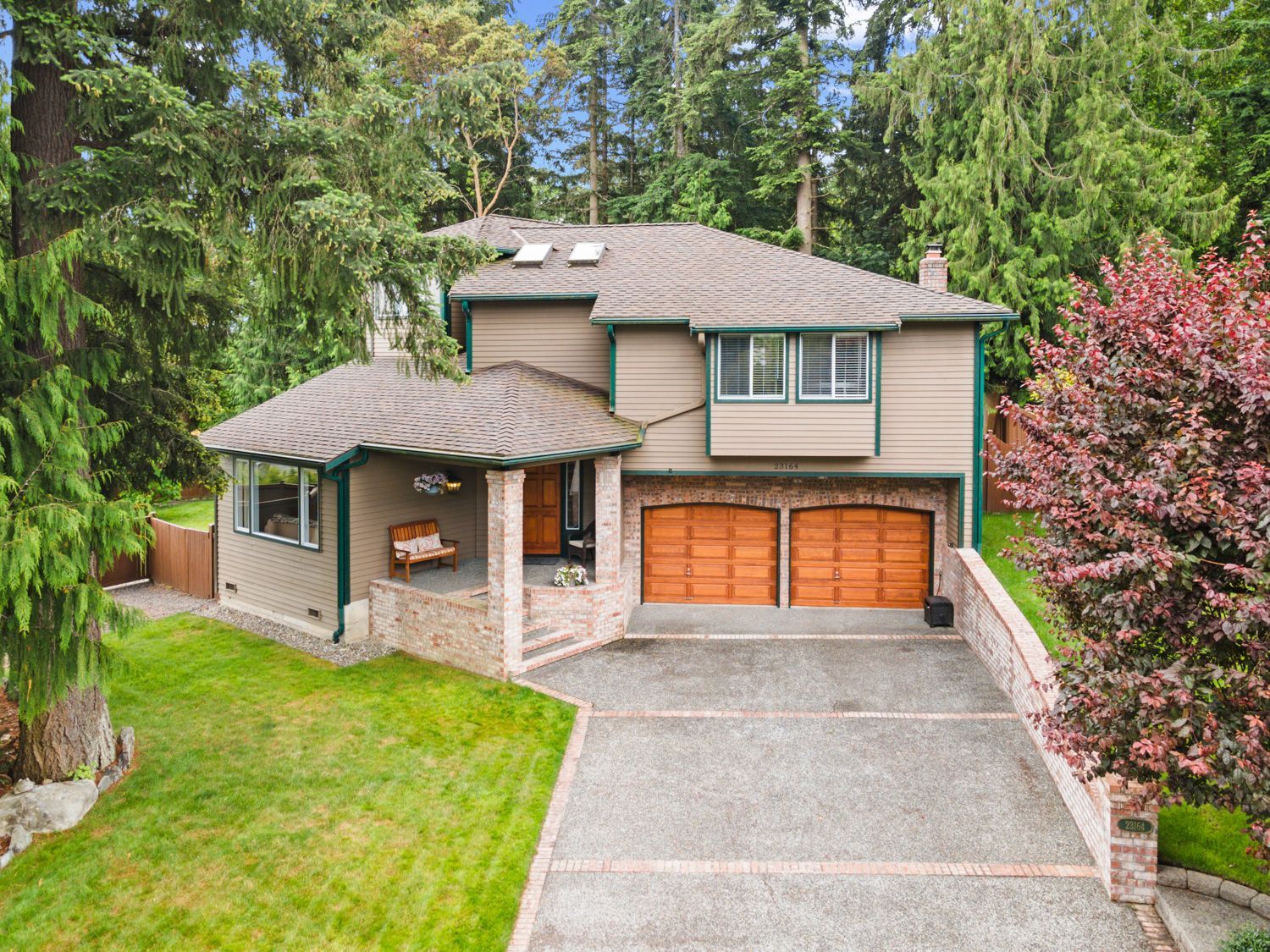 An drone shoot of a house with wood garage doors with a driveway leading to it surrounded by trees. Shoot by Hometrack and Team.