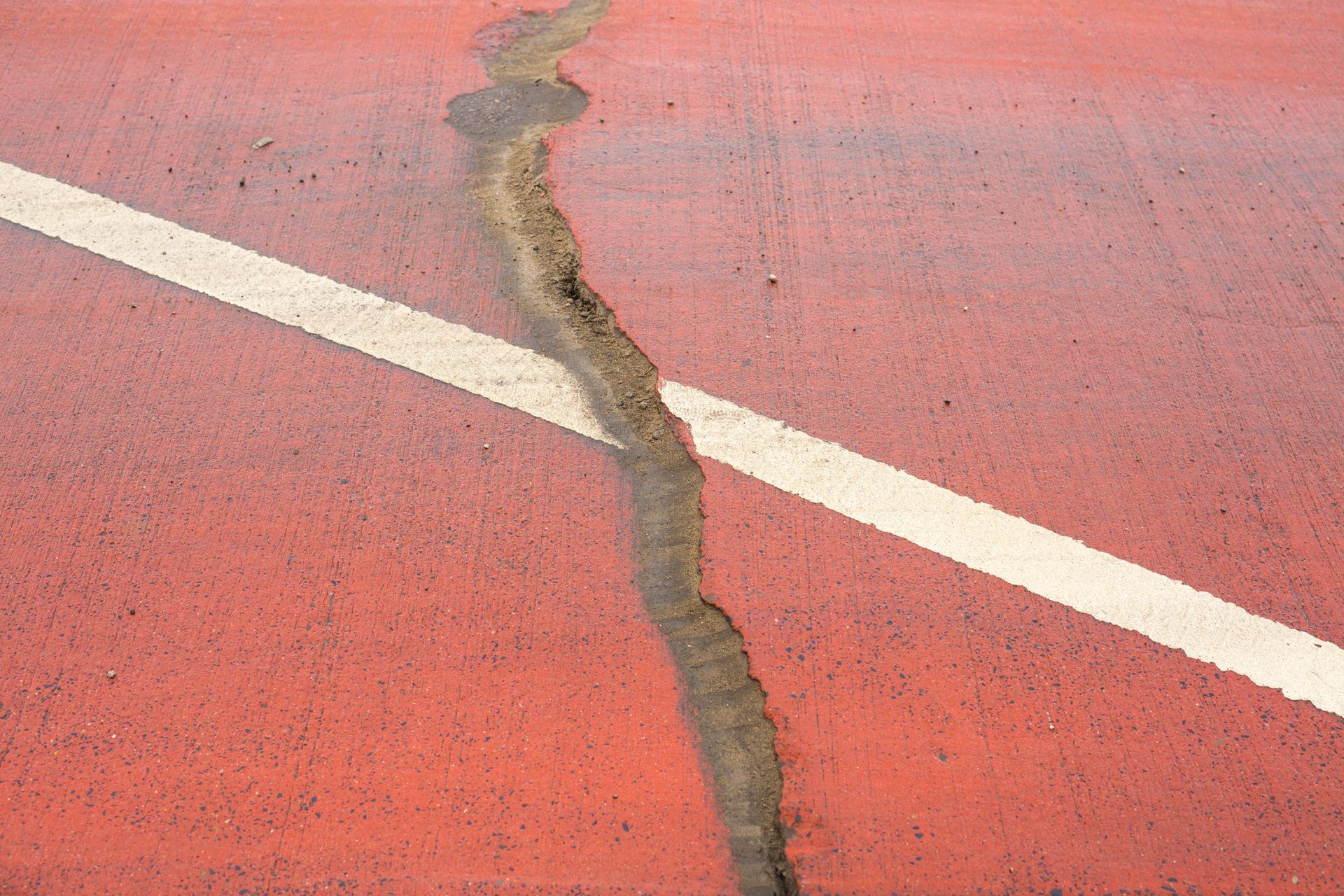 Cracked concrete surface near a building wall, showing damage and disrepair.